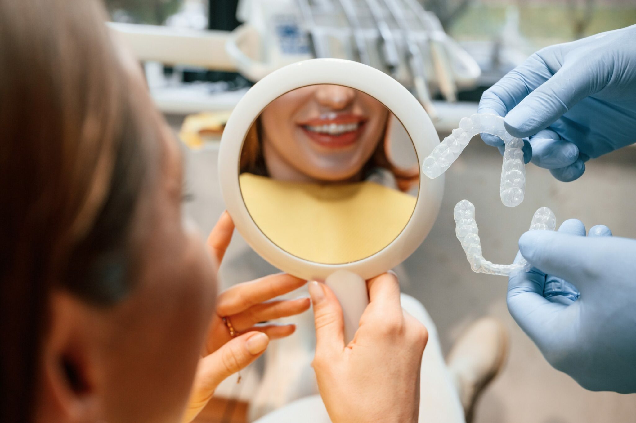 Patiente usant un miroir pour découvrir ses aligneurs présentés par l'orthodontiste